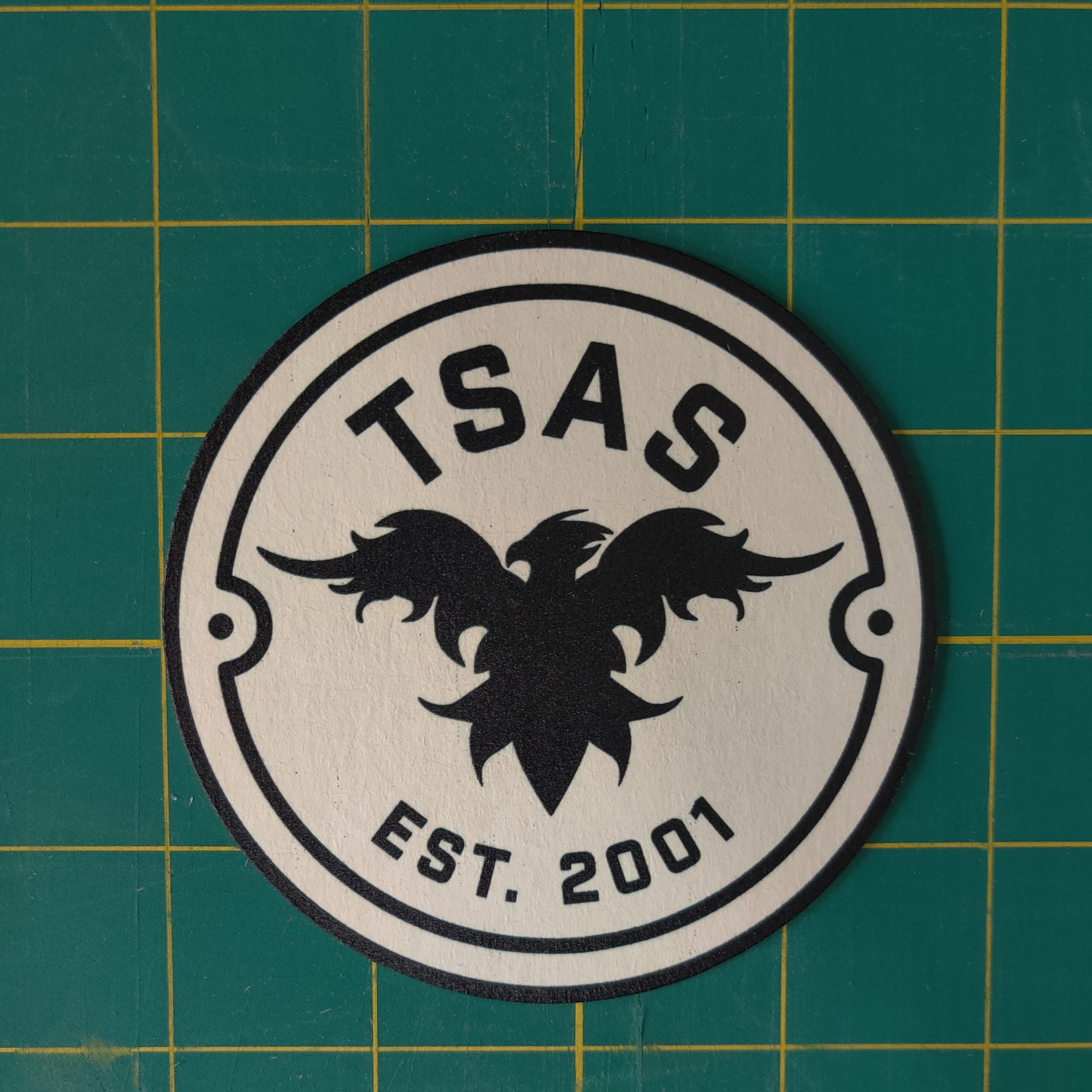Round, white coaster with TSAS logo in black